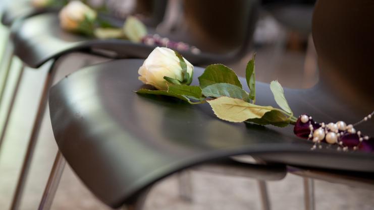 Weißer Rosenbogen mit Blättern und Perlen auf schwarzem Stuhl bei einer Veranstaltung.