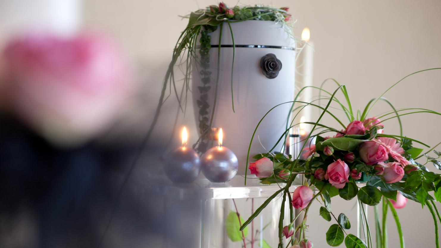 Blumenschmuck mit rosa Rosen und grünen Pflanzenarrangements auf einem Tisch, umgeben von Kerzen und einem weißen Behälter.
