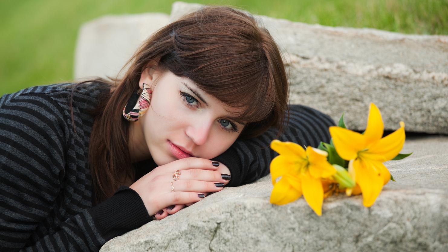 Junge Frau mit Blumen in der Nähe, die auf einem Stein liegt und in die Kamera schaut. Hintergrund mit grünem Gras.