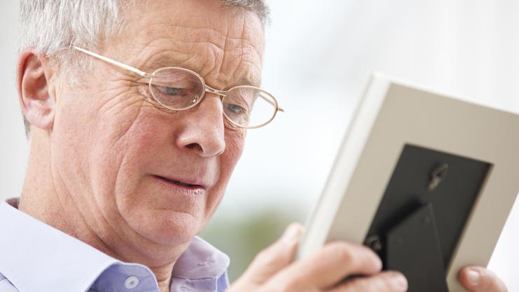 Ein älterer Mann mit Brille betrachtet ein Foto in einem Bilderrahmen.