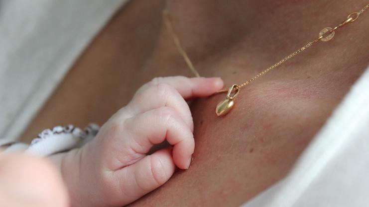 Babyhand greift sanft nach einer goldenen Halskette mit Anhänger auf der Haut einer Person.